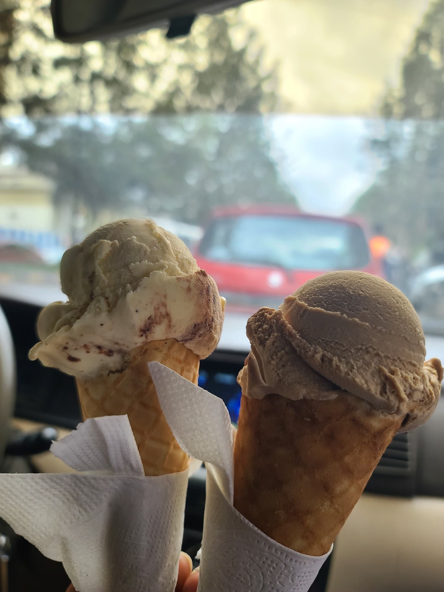 Two delicious gelato scoops in waffle cones held inside a vehicle